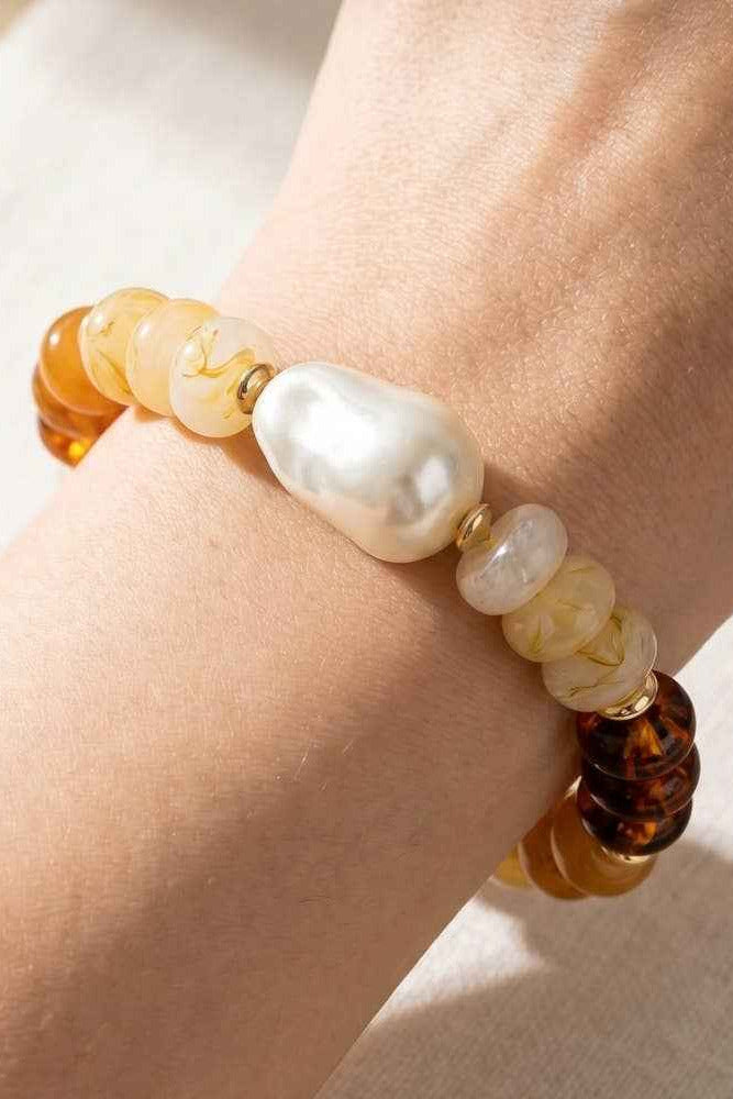 Beaded bracelet with pearls and tortoiseshell beads on a wrist against a neutral background