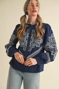 Woman wearing a navy blouse with white embroidery on a beige background