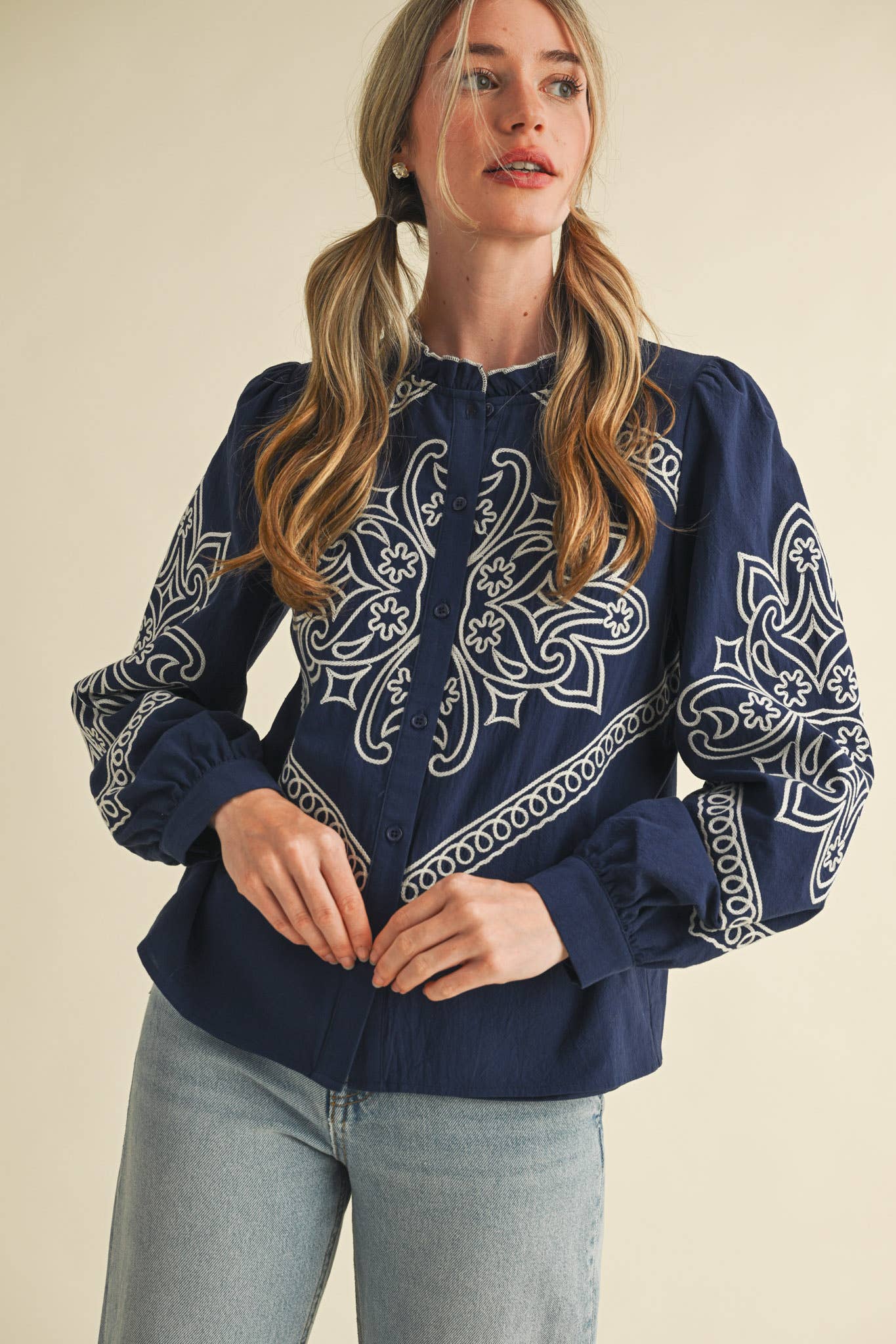 Woman wearing a navy blouse with white embroidery on a beige background