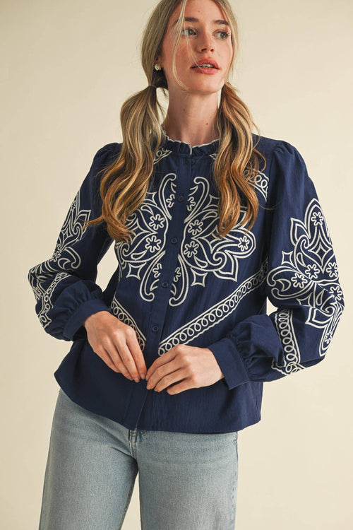 Woman wearing a navy blouse with white embroidery on a beige background