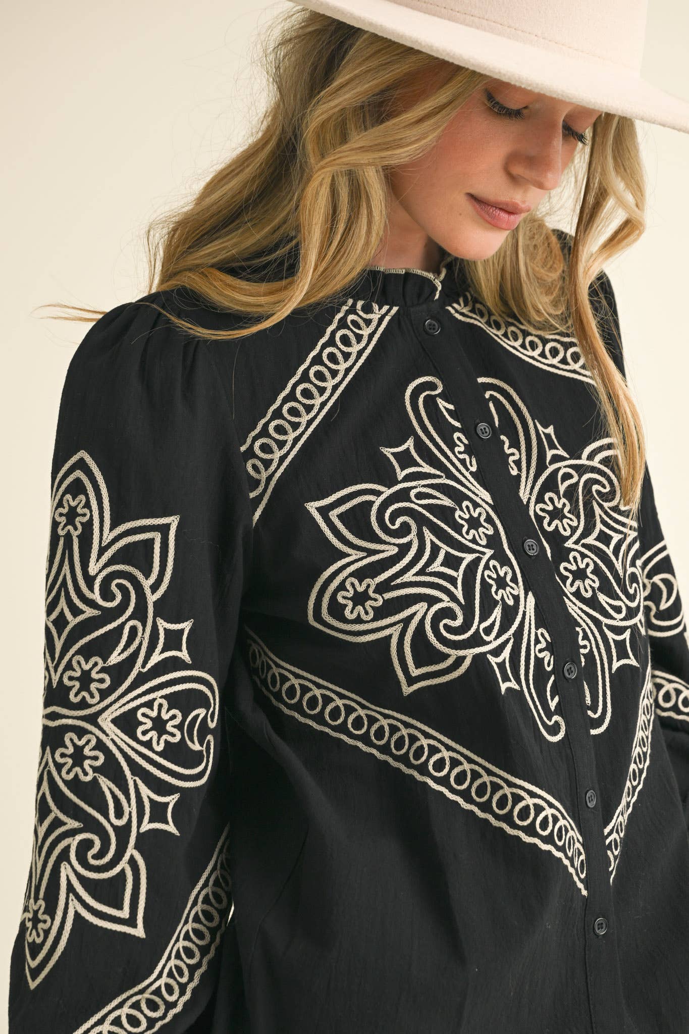 Black blouse with white intricate patterns worn by a person against a neutral background