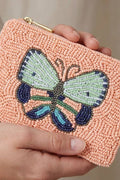 Peach-colored beaded clutch with a butterfly design held by a hand against a neutral background
