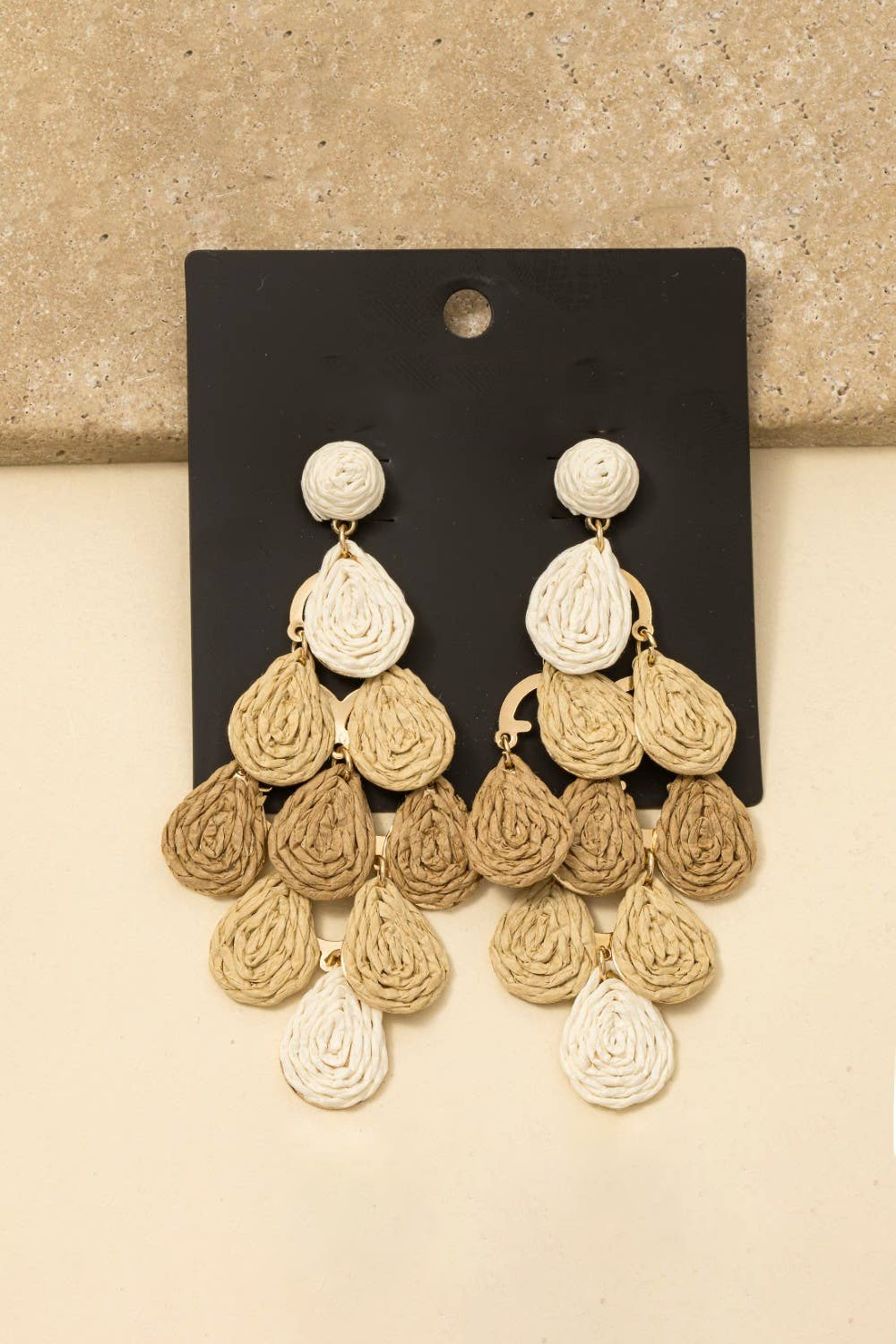 Pair of gold and beige chandelier earrings on a black card against a beige background