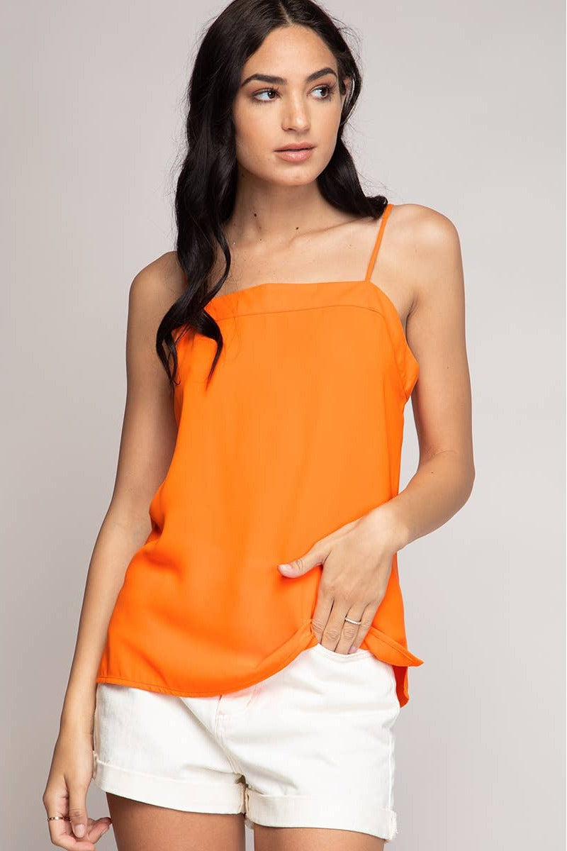 Woman wearing an orange top and white shorts on a plain background