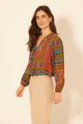 Woman wearing a colorful patterned blouse with beige pants on a plain background