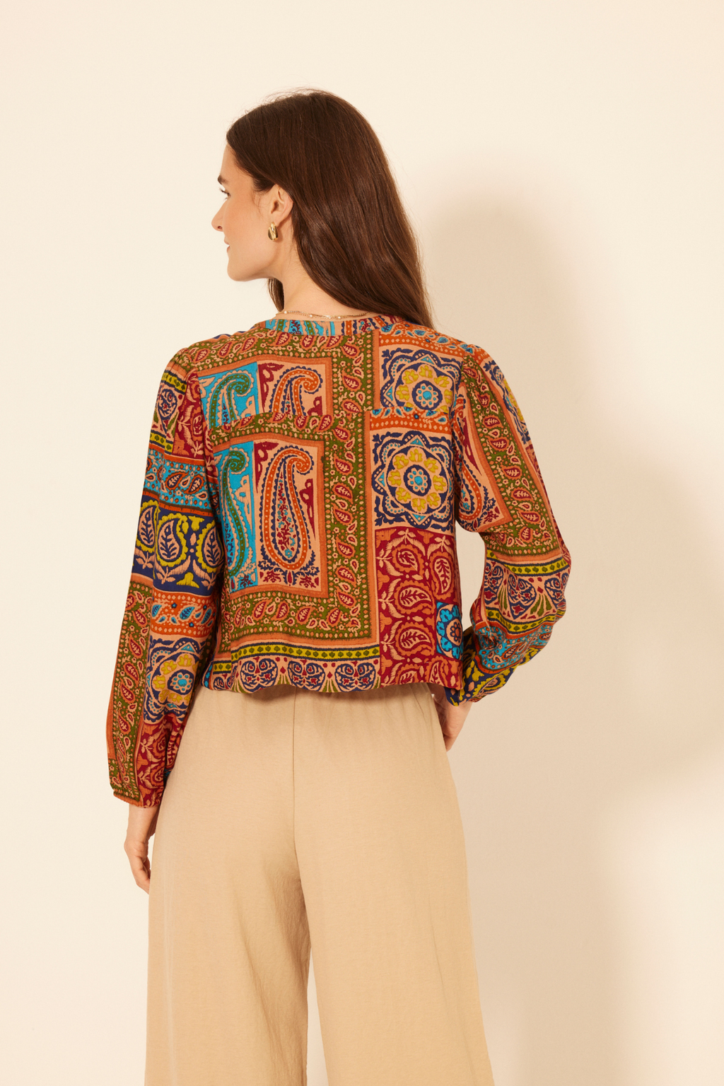 Woman wearing a colorful patterned top with beige pants on a plain background