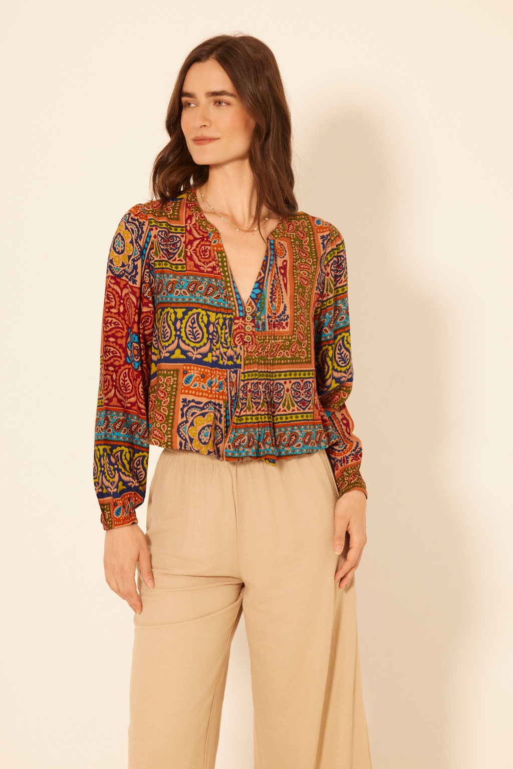 Woman wearing a colorful patterned blouse and beige pants on a plain background