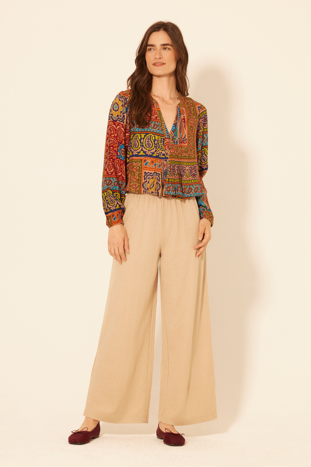 Woman wearing a patterned blouse and beige pants on a plain background