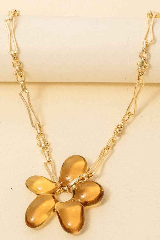Gold necklace with a flower-shaped pendant on a beige background