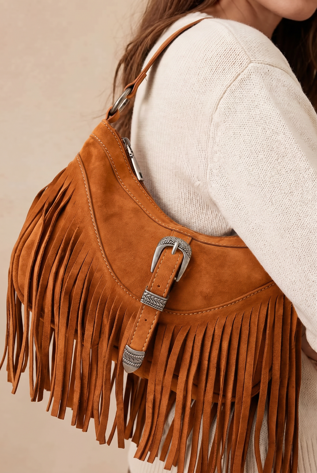 Brown suede handbag with fringe and a silver buckle, worn by a person.