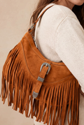 Brown suede handbag with fringe and a silver buckle, worn by a person.