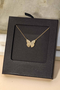Gold butterfly necklace in a black jewelry box on a light wooden surface