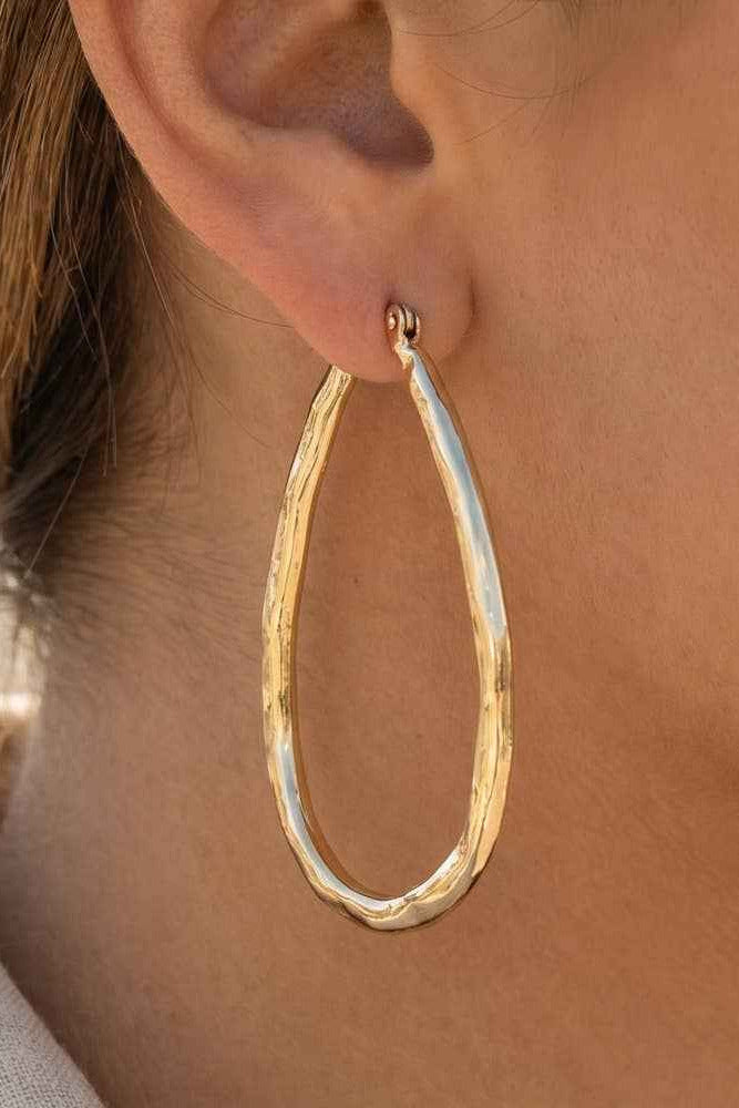 Gold hoop earring worn by a person with a blurred background