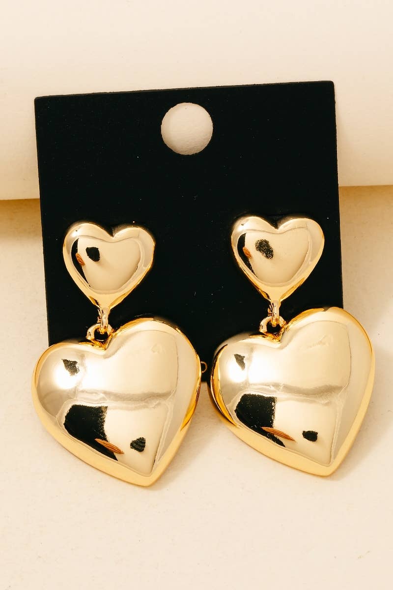 Gold heart-shaped earrings on a black card with a beige background