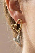 Gold and silver heart-shaped earrings worn by a person.