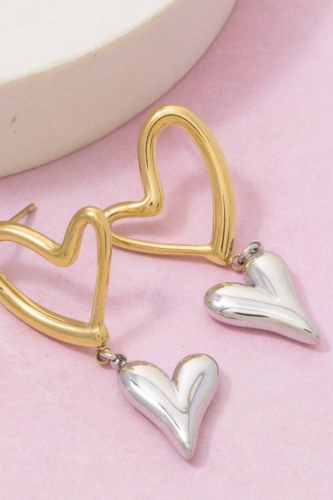 Gold and silver heart-shaped earrings on a pink background