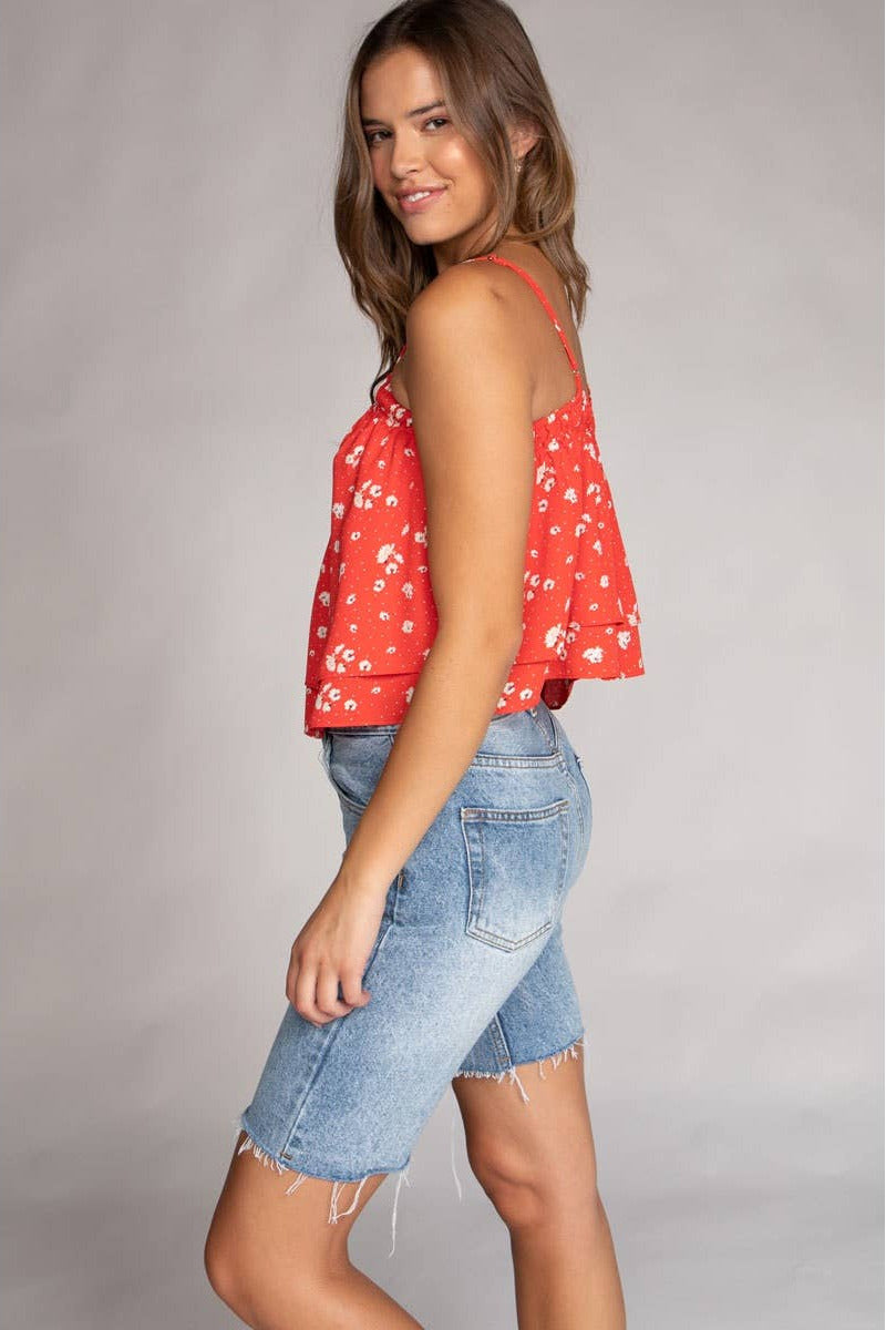 Woman wearing a red floral top and denim shorts on a gray background