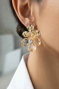 Gold floral earring worn by a person with a blurred background