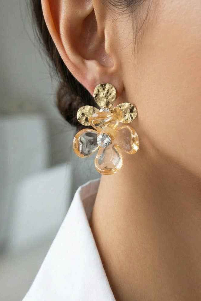 Gold floral earring worn by a person with a blurred background