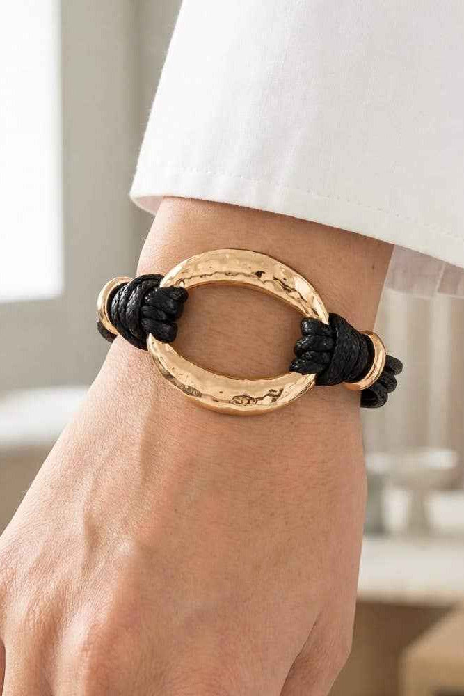 Gold and black bracelet on a wrist with a blurred indoor background