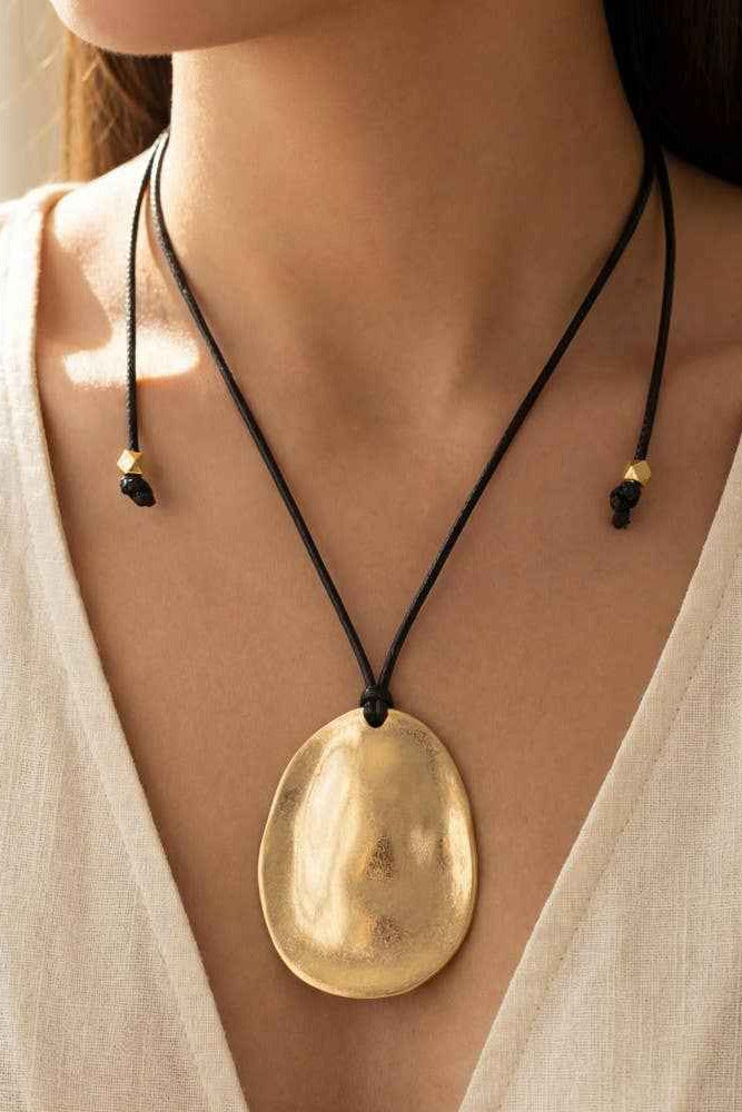 Gold pendant necklace on a person wearing a white top