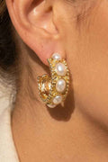 Close-up of an ear wearing a gold earring with pearl-like stones.