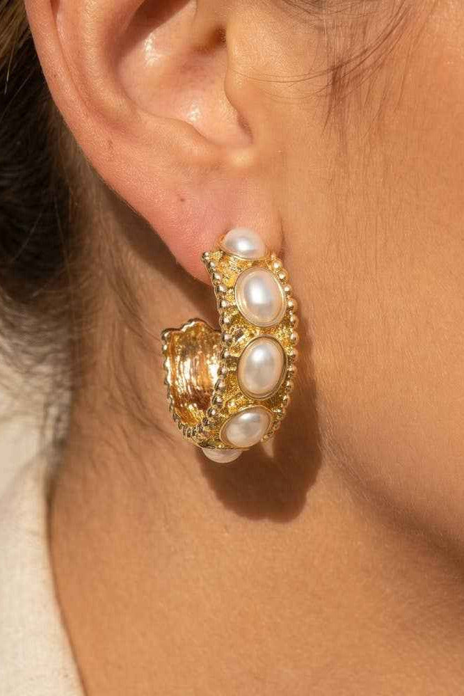 Close-up of an ear wearing a gold earring with pearl-like stones.