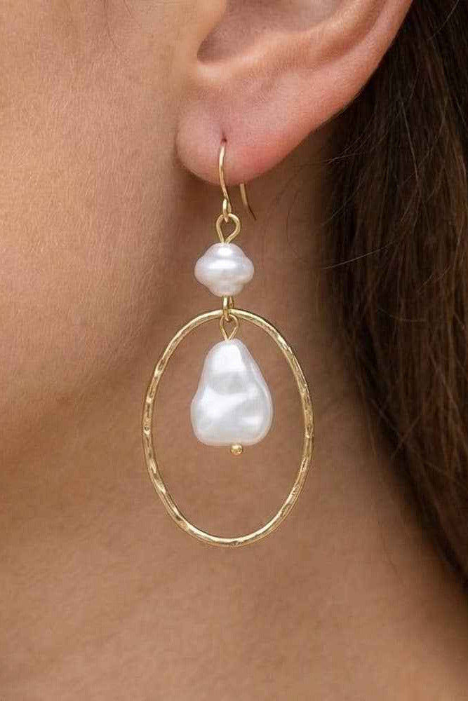 Gold hoop earrings with baroque pearls worn by a person.