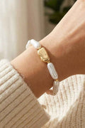 Bracelet with gold and pearl beads on a wrist, wearing a beige sweater.