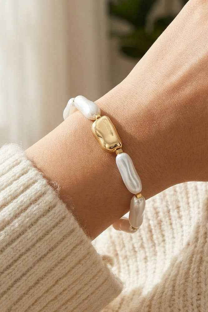 Bracelet with gold and pearl beads on a wrist, wearing a beige sweater.