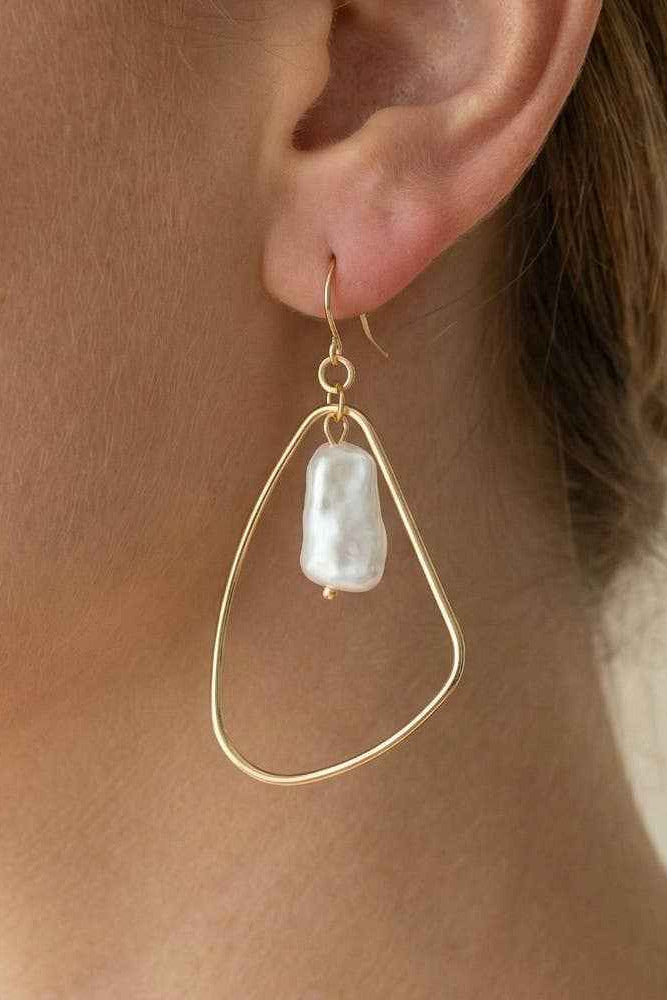 Gold earring with a pearl drop worn by a person