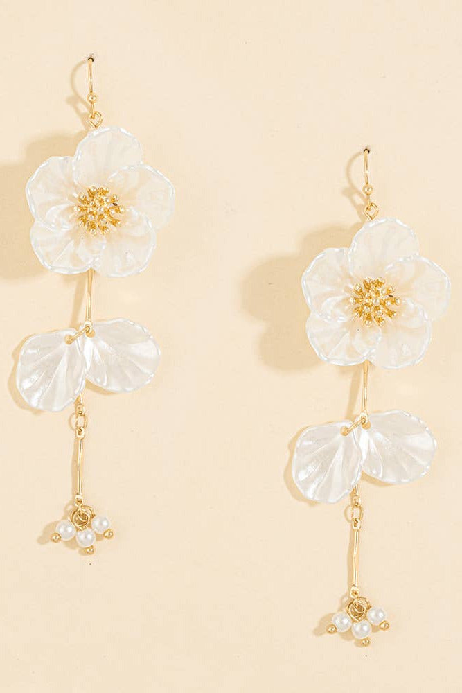 A pair of gold-tone dangle earrings featuring large white flower charms, two translucent white petal charms, and small pearl clusters at the bottom, displayed on a warm beige background.
