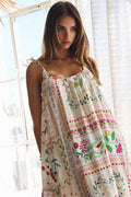 Woman wearing a floral patterned dress standing in a bright room with large windows.