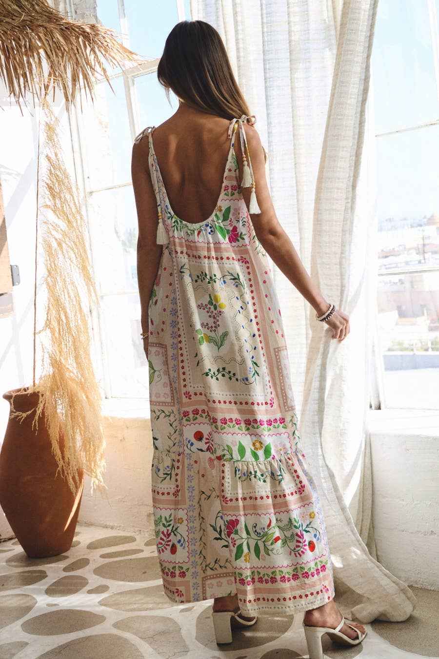 Woman wearing a floral dress standing in a bright room with large windows.