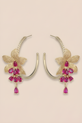 Gold hoop earrings with pink gemstones on a beige background
