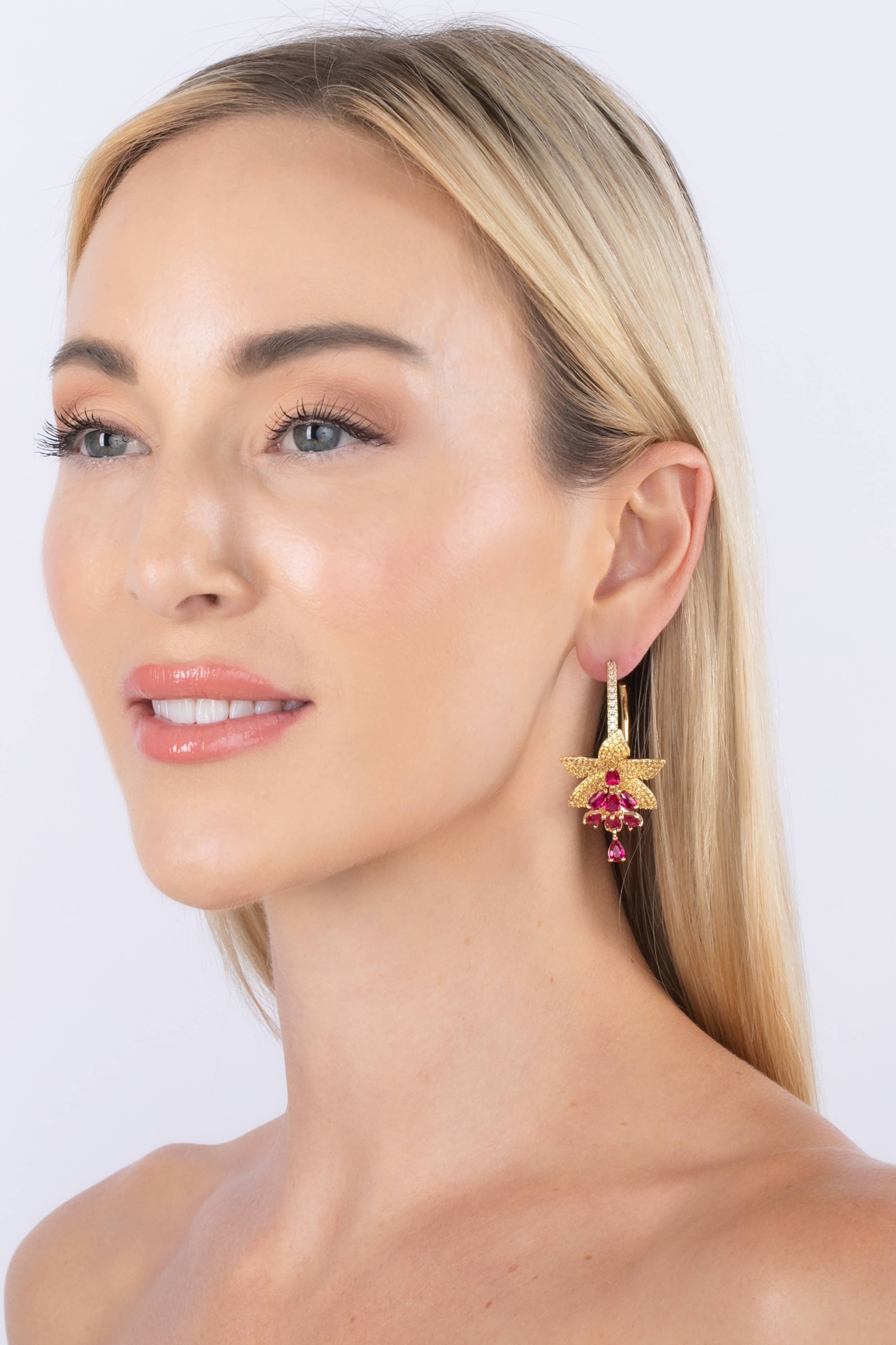 Close-up of a woman wearing gold earrings with red gemstones on a white background