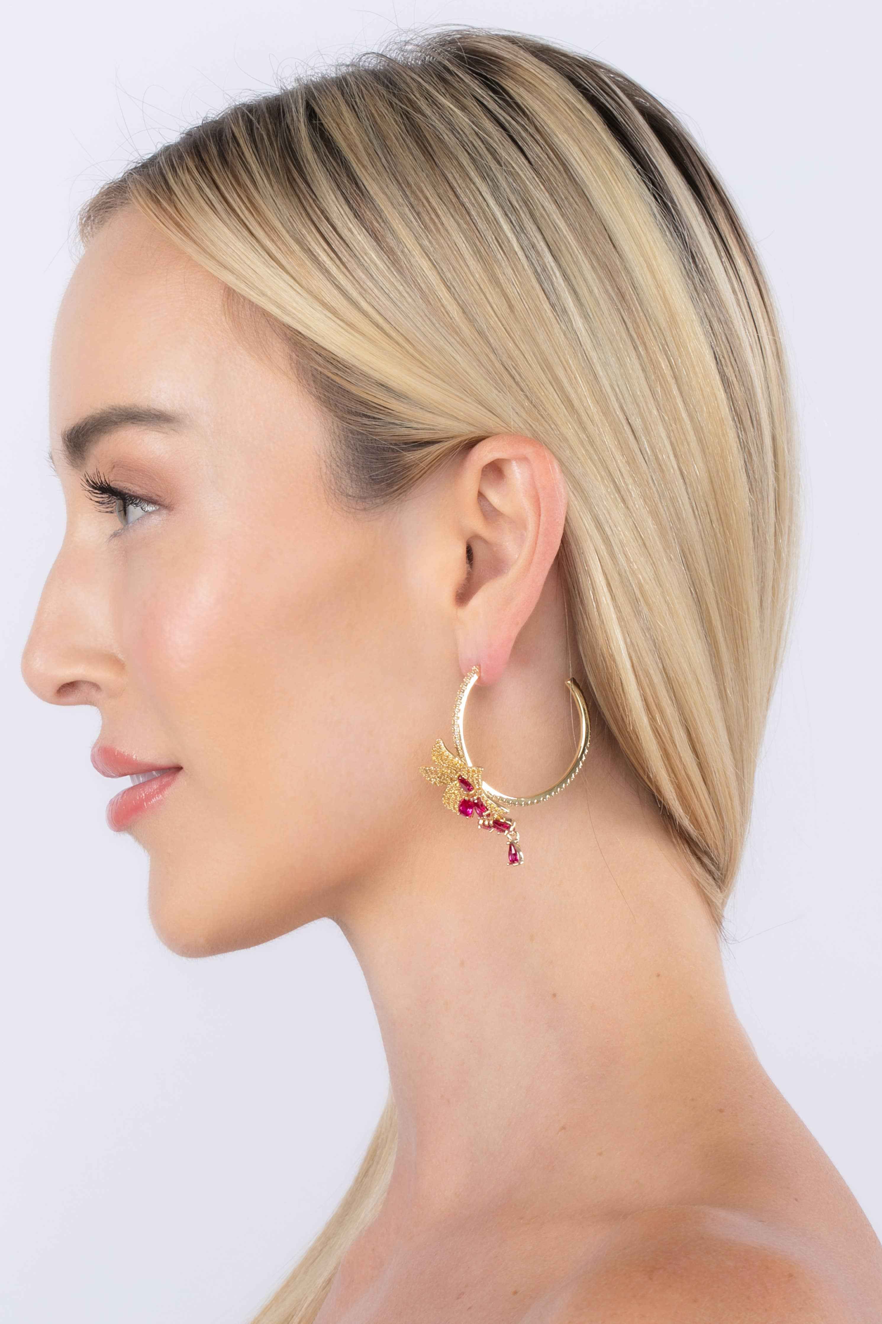 Woman wearing gold hoop earrings with red gemstones on a white background