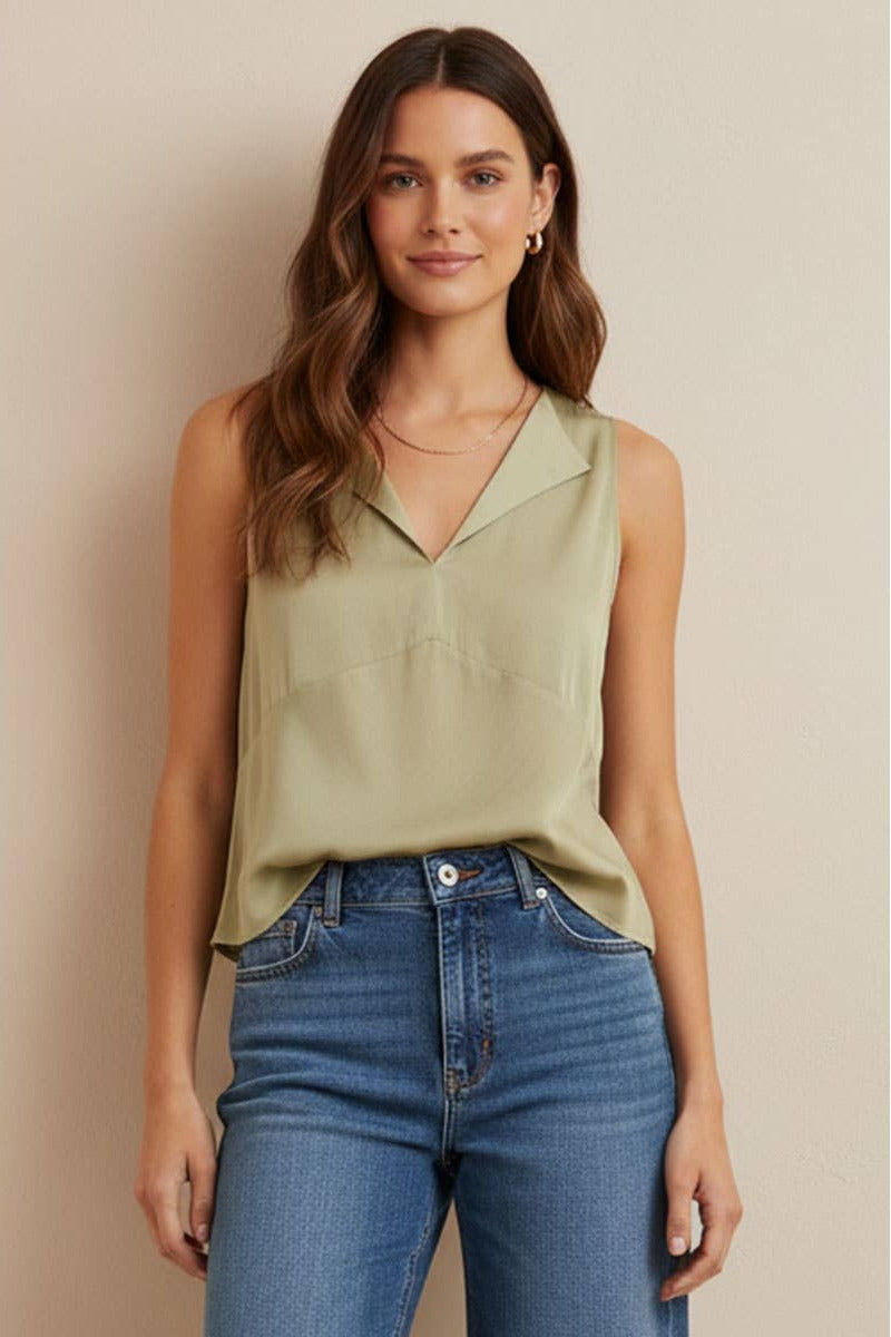 Woman wearing a light green sleeveless top and blue jeans against a beige background