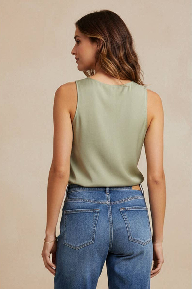 Woman wearing a green sleeveless top and blue jeans against a beige background