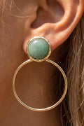 A close-up of a gold hoop earring with a round green stone stud, worn on a person's ear.