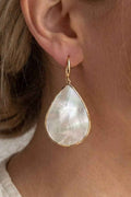 Teardrop-shaped earring with gold frame worn by a person
