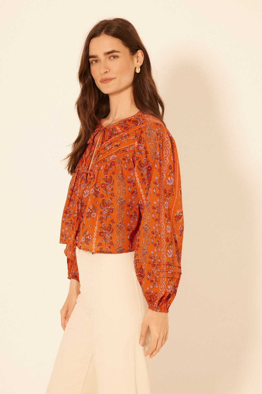 Woman wearing an orange patterned blouse against a beige background