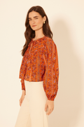 Woman wearing an orange patterned blouse against a beige background