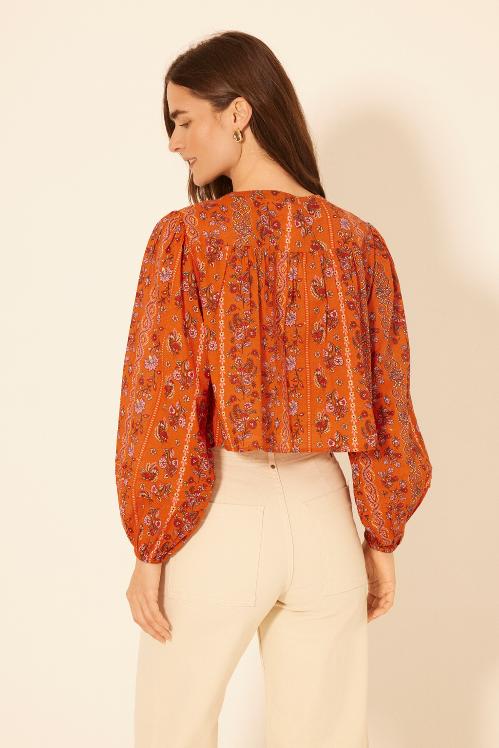 Woman wearing an orange floral blouse against a beige background