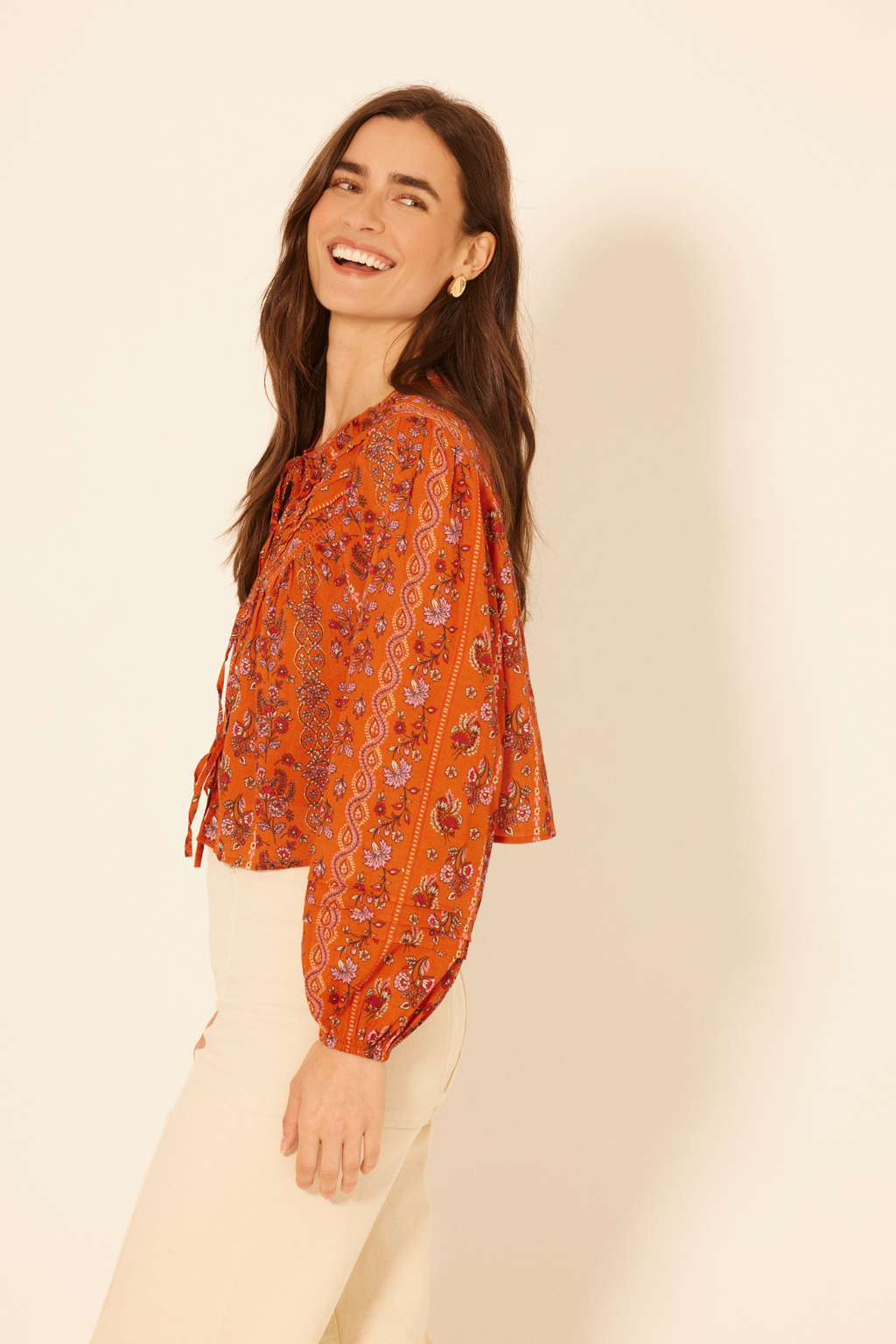 Woman wearing an orange patterned blouse against a beige background