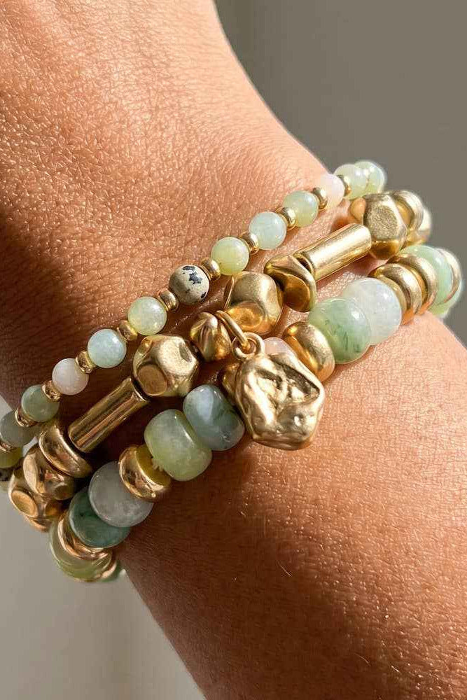 Stack of gold and green beaded bracelets on a wrist with a neutral background