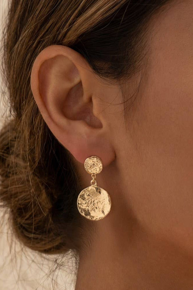 Close-up of a person wearing gold earrings with a blurred background