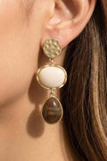 Close-up of a woman wearing gold earrings with white and brown stones.