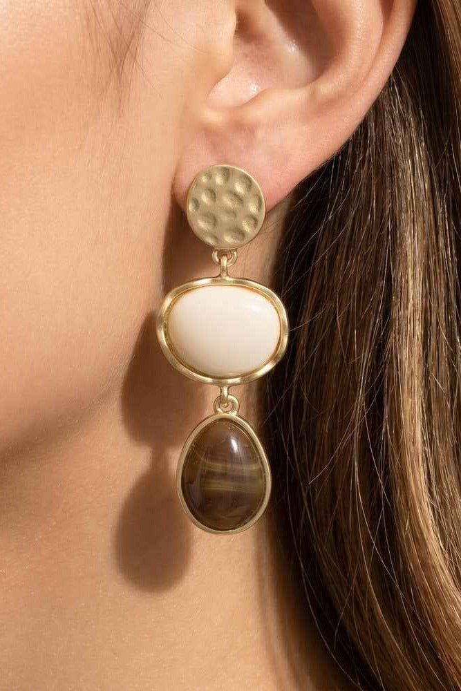 Close-up of a woman wearing gold earrings with white and brown stones.