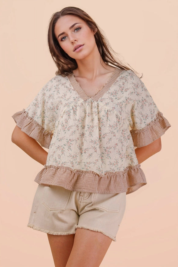 Woman wearing a floral blouse with ruffled sleeves and shorts on a peach background